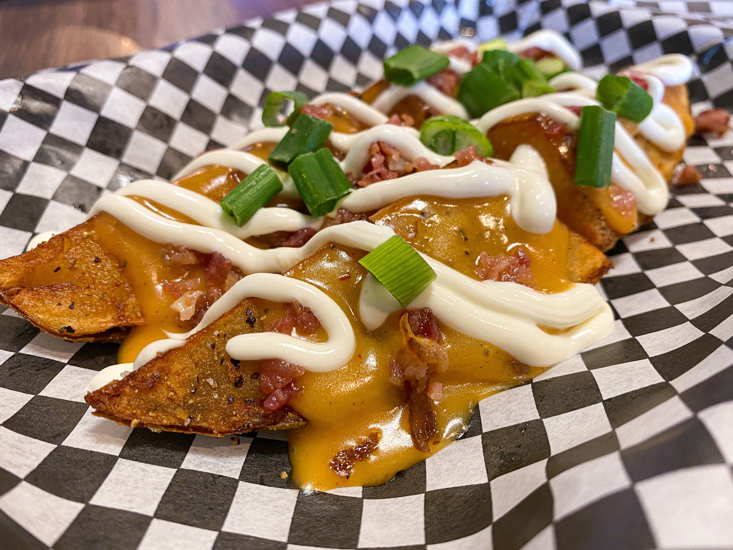 Loaded potato wedges: fried and baked potato wedges seasoned. Wedges are drizzled nacho cheese and sour cream with bacon bits and green onions to garnish.